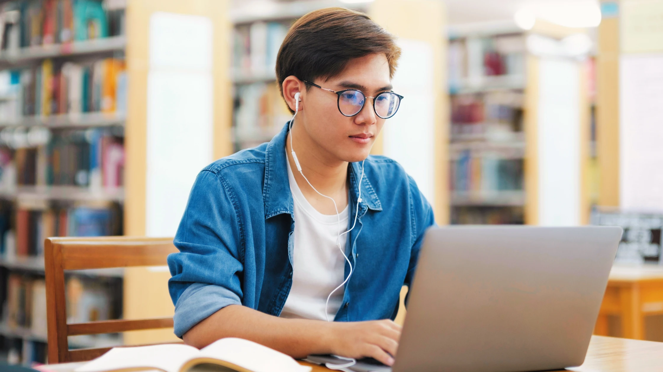 Medical student studying on a laptop in the library with earphones in, preparing for USMLE Step 1.