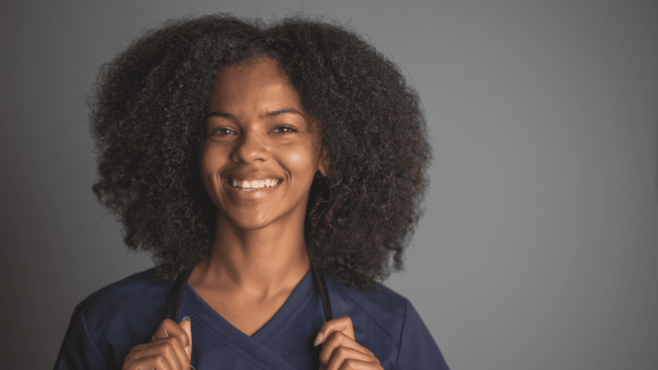 A medical resident wearing scrubs and holding a stethoscope around her neck.